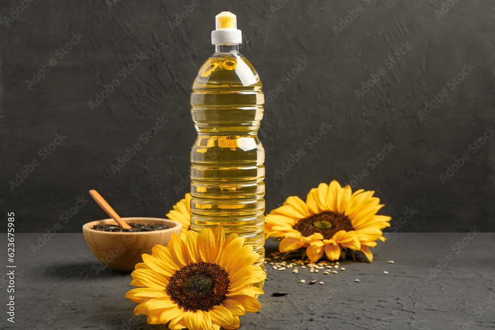 Sunflowers, seeds and bottle of oil on black background