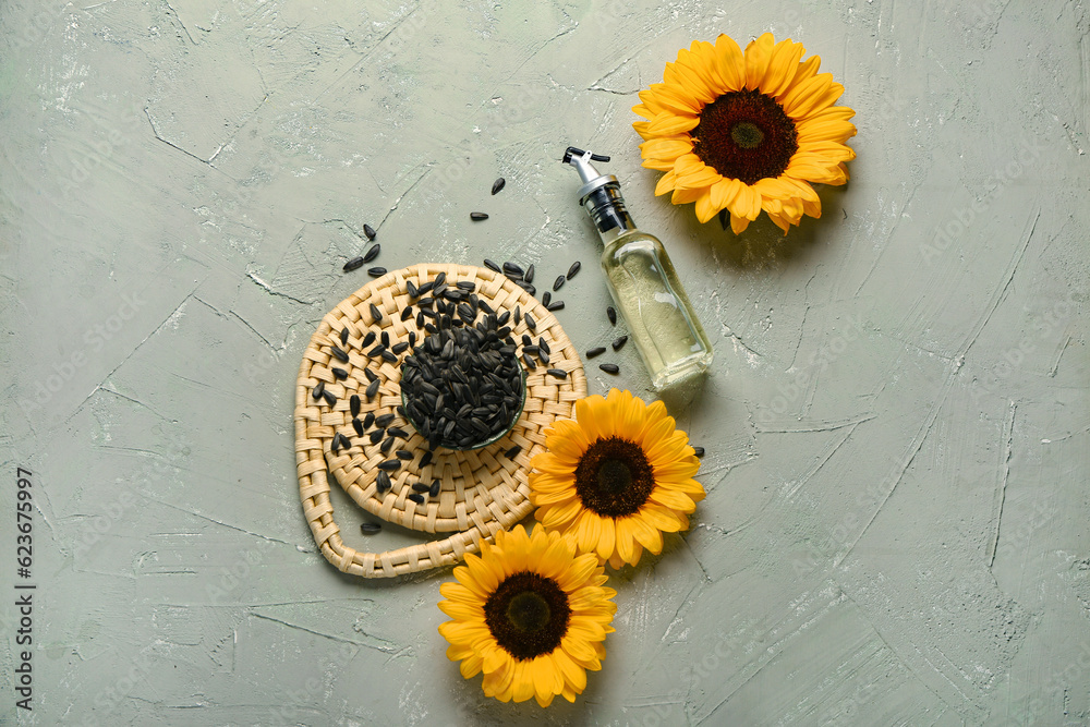 Sunflowers, seeds and bottle of oil on green background