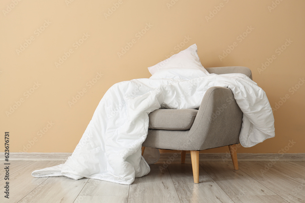 Grey armchair with white blanket and pillow near beige wall