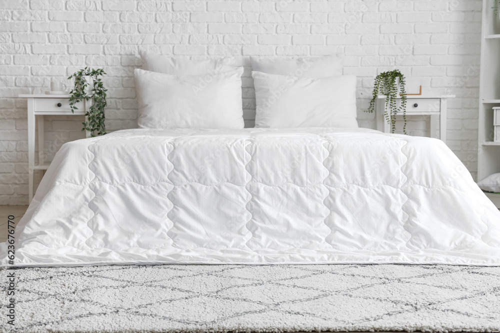 Cozy bed with white blanket and pillows in interior of light bedroom