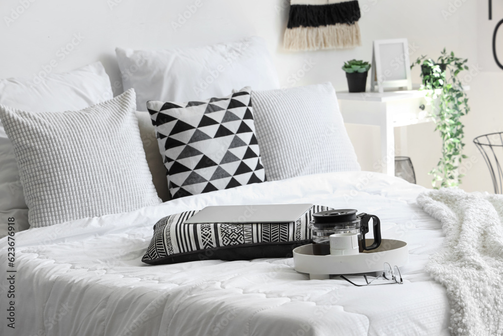 Tray with coffee maker, cup and modern laptop on white blanket in bed, closeup