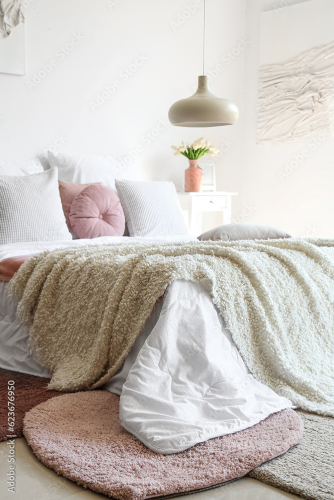 Cozy bed with white blanket and pillows in interior of light bedroom