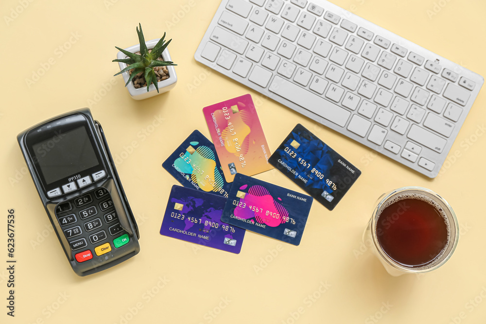 Keyboard with payment terminal, cup of coffee and credit cards on pale yellow background