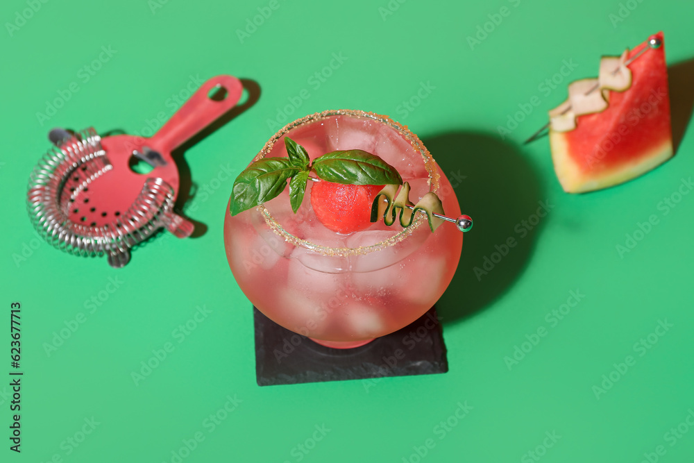 Glass of tasty watermelon cocktail with strainer on green background