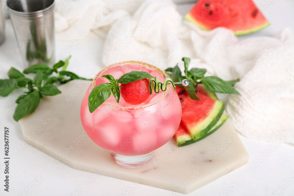 Board with glass of tasty watermelon cocktail, shaker and mint on white table