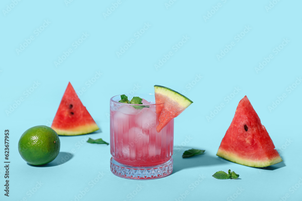 Glass of tasty watermelon cocktail with mint and lime on blue background