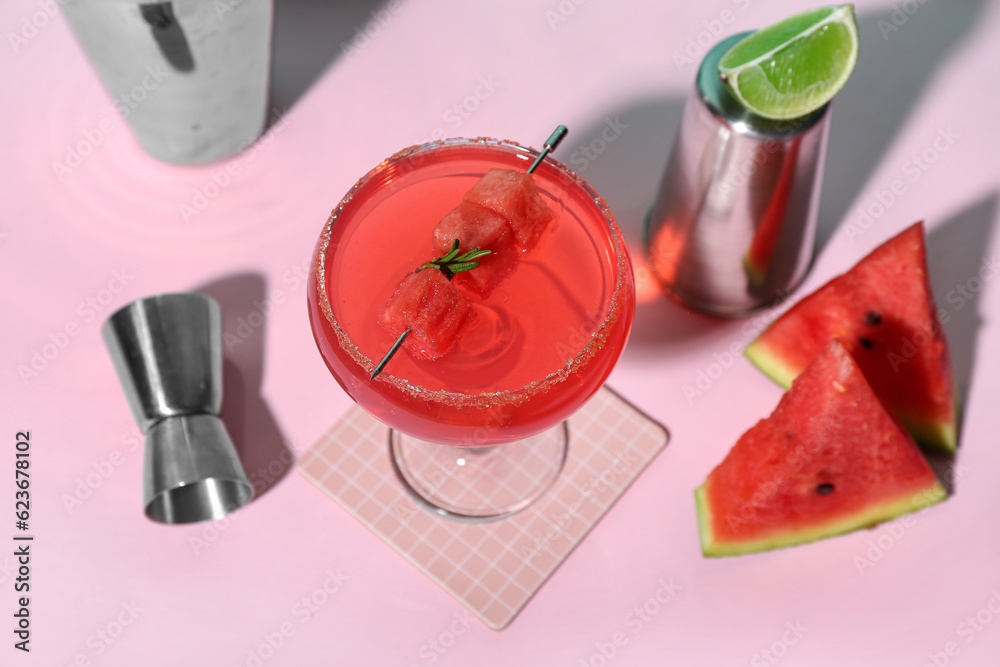 Glass of tasty watermelon cocktail with shakers and jigger on pink background