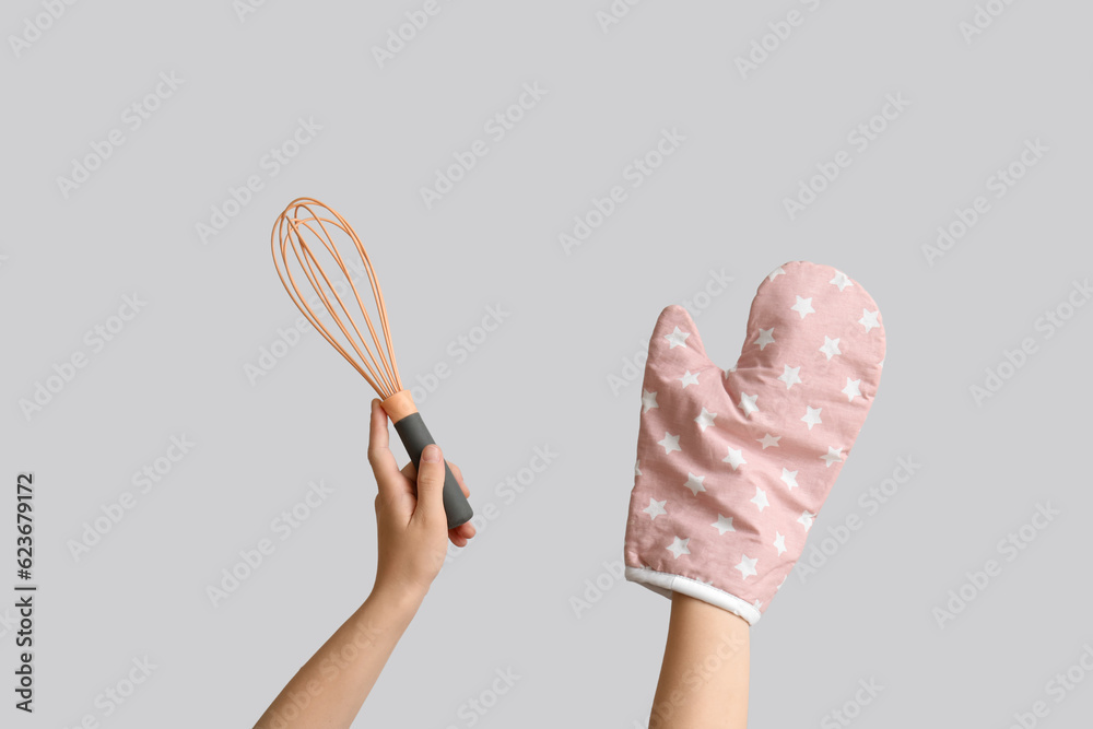 Female hands with whisk and mitten on grey background