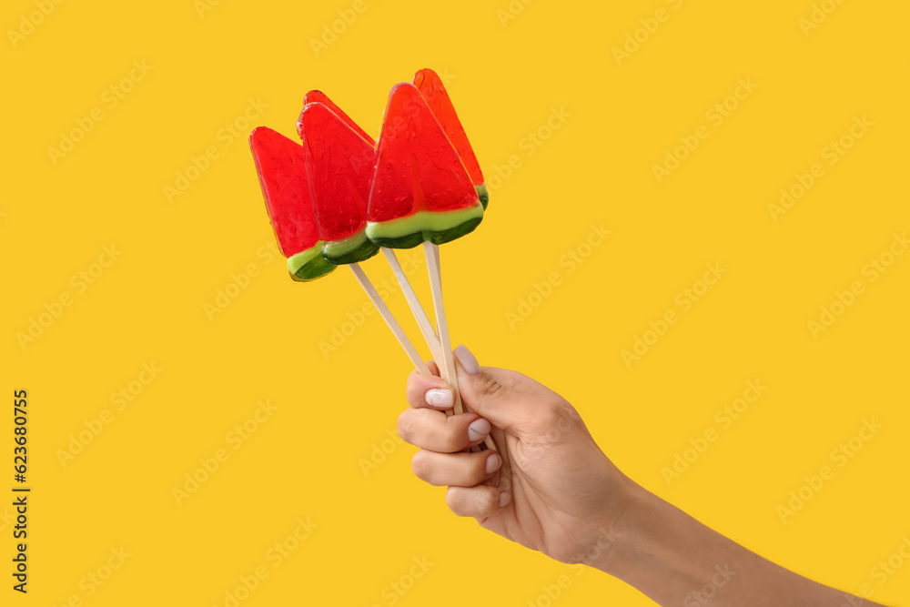 Woman holding lollipops in shape of watermelon slice on yellow background