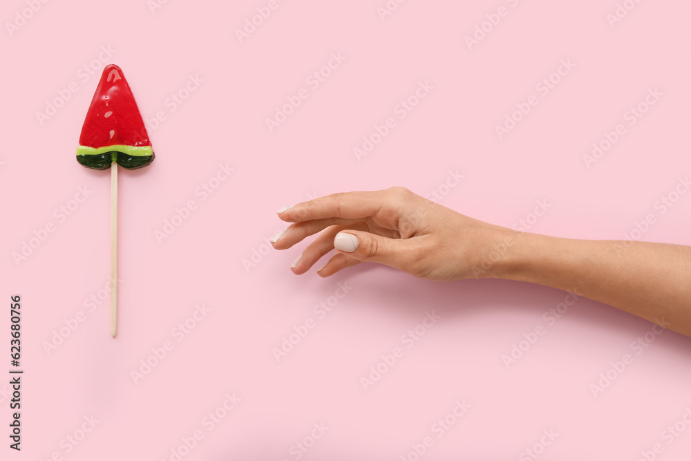 Female hand with lollipop in shape of watermelon slice on pink background