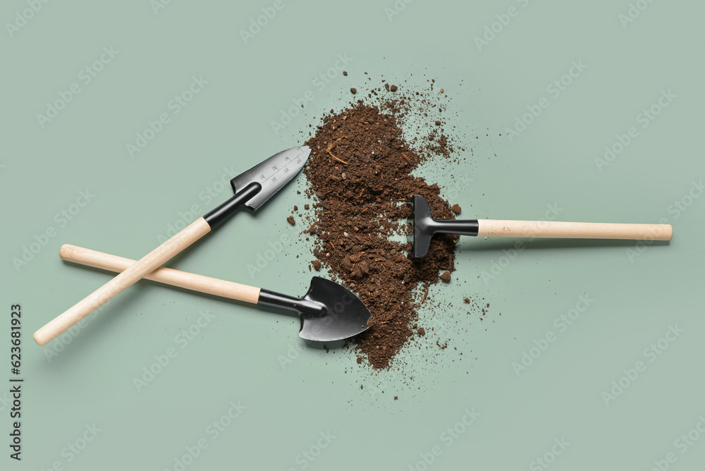 Gardening rake, shovels and soil on green background