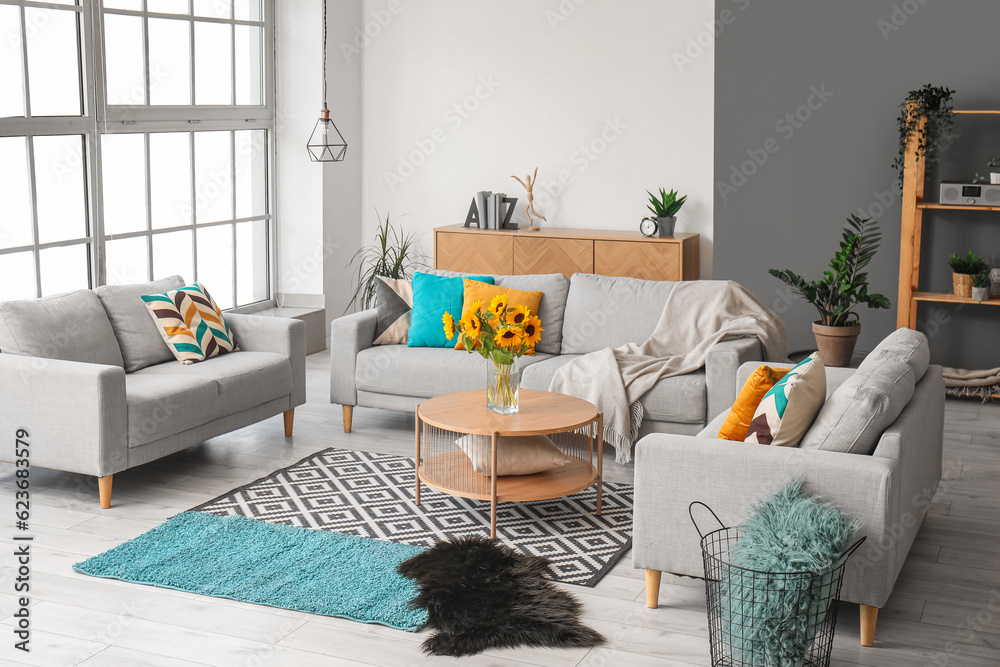 Cozy grey sofas and vase with beautiful sunflowers in interior of light living room