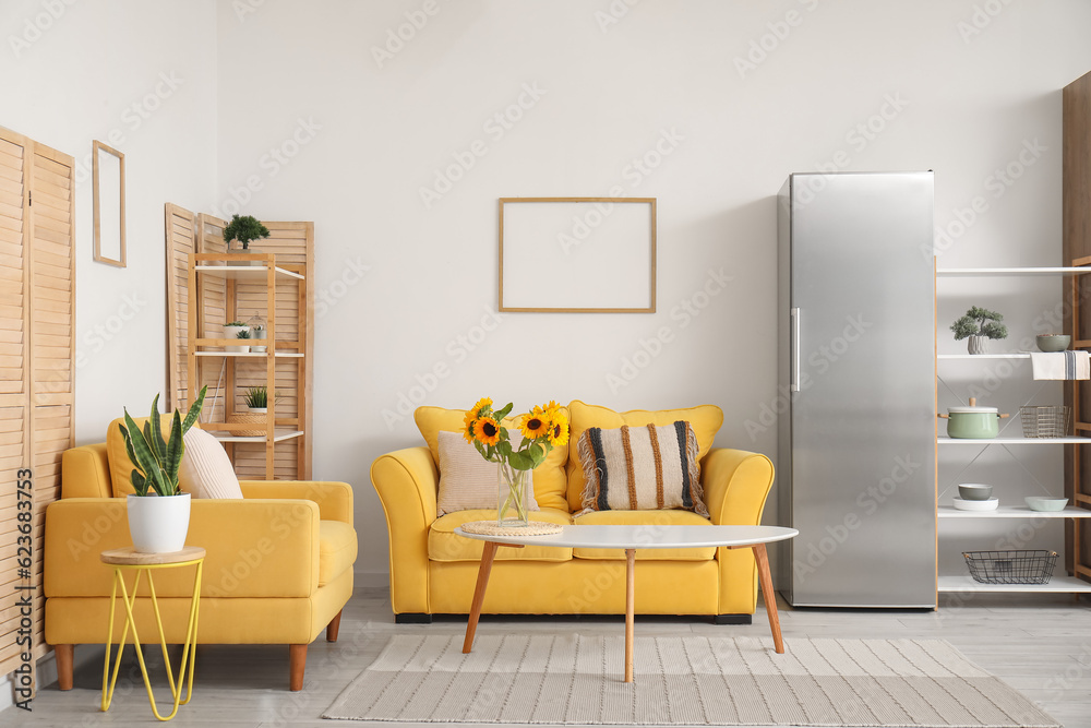 Vase with beautiful sunflowers, yellow sofa and armchair in interior of stylish living room