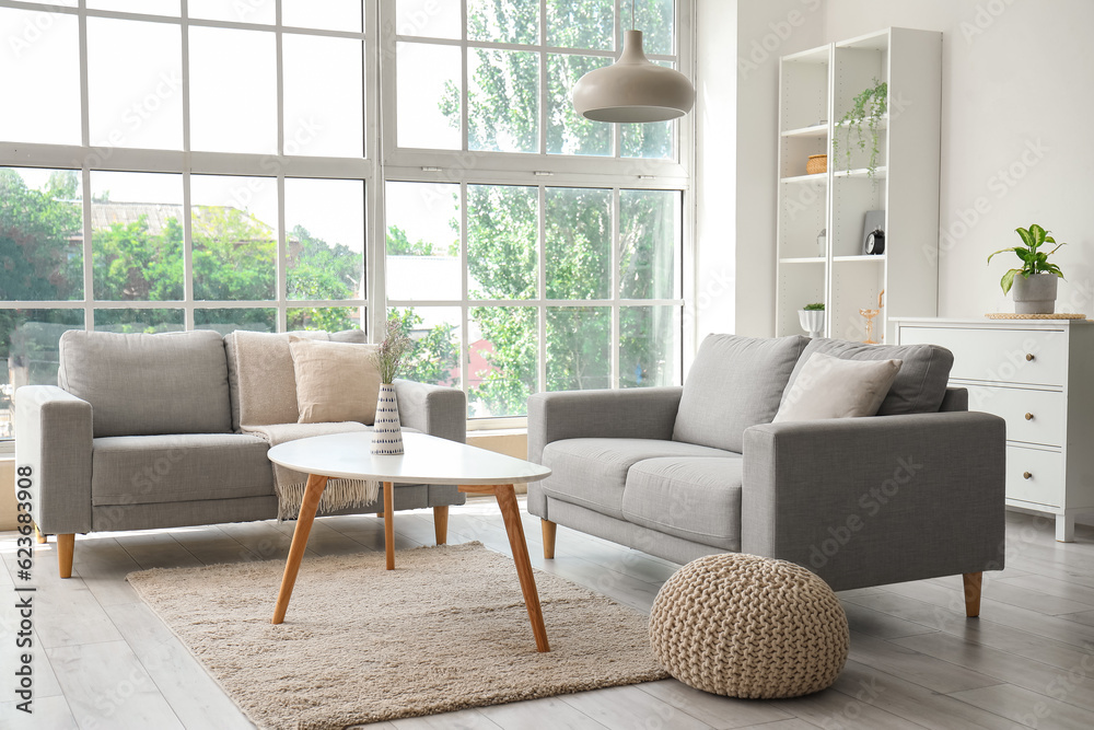 Interior of light living room with cozy grey sofas, coffee table and big window