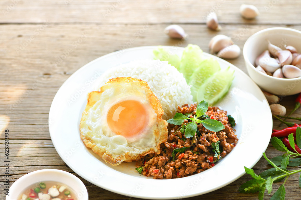 Rice topped with stir-fried pork, basil and fried egg on wooden table.