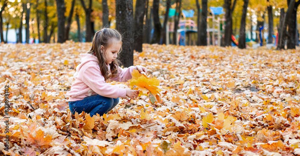 Positive little girl playing in the autumn park. Happy emotional child catches maple leaves and laug