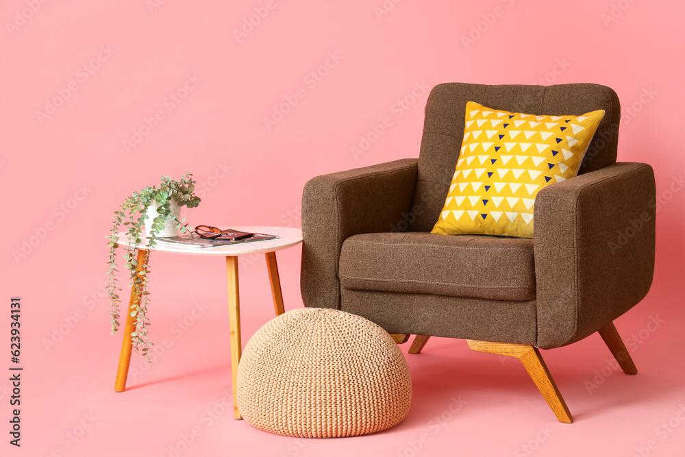 Brown armchair with pouf and table on pink background