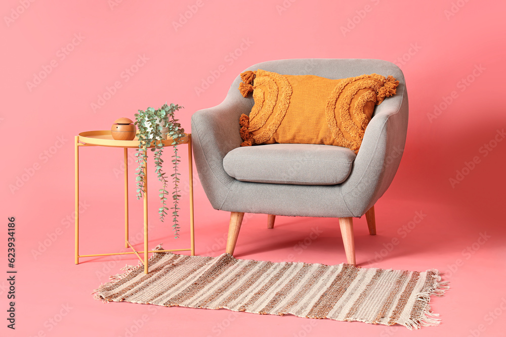 Grey armchair with table and rug on pink background