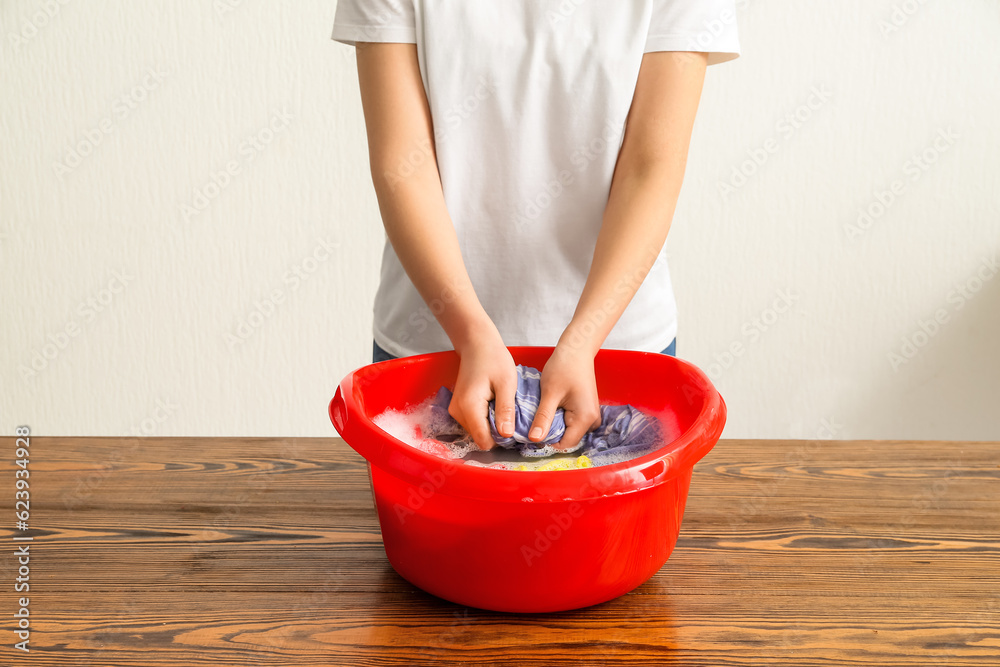 Woman washing laundry in plastic basin on wooden table