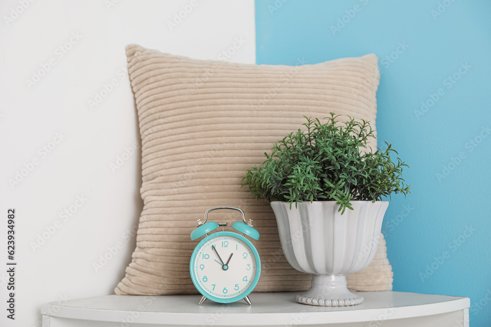 Vintage alarm clock with houseplant and pillow on shelf in room