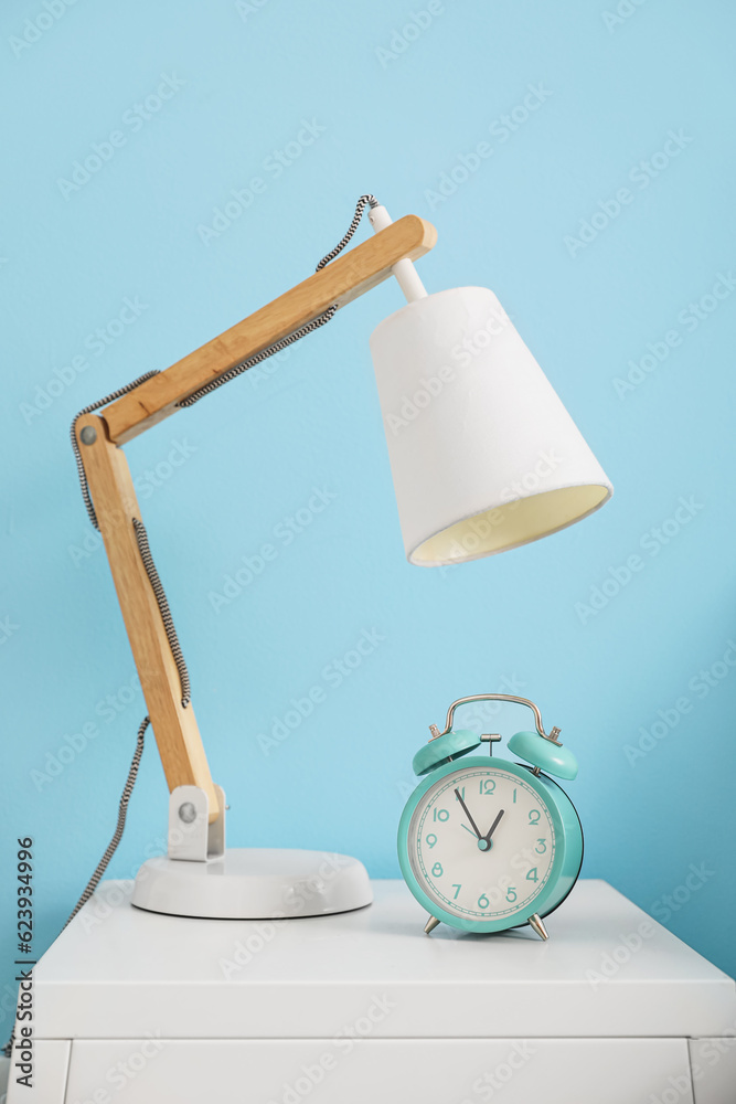 Vintage alarm clock with lamp on table near blue wall