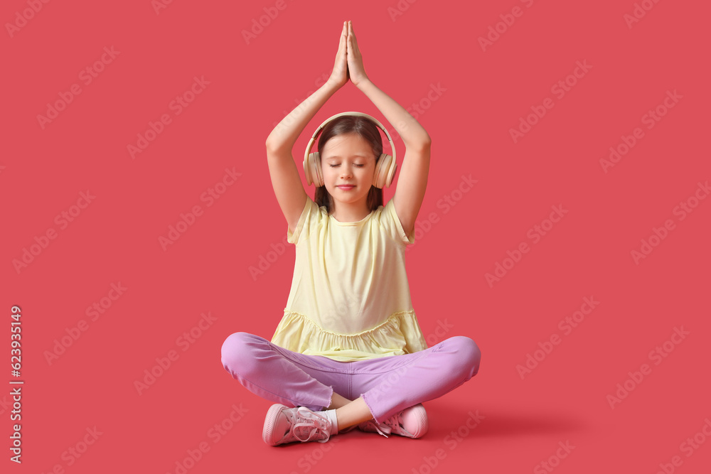 Little girl in headphones meditating on red background