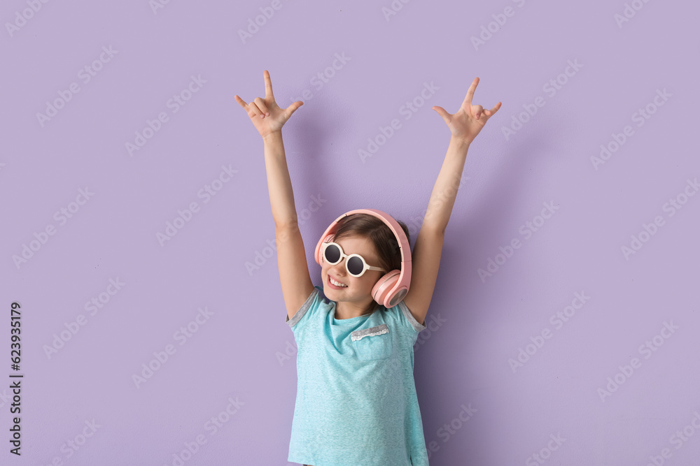 Little girl in headphones showing  devil horns  on lilac background