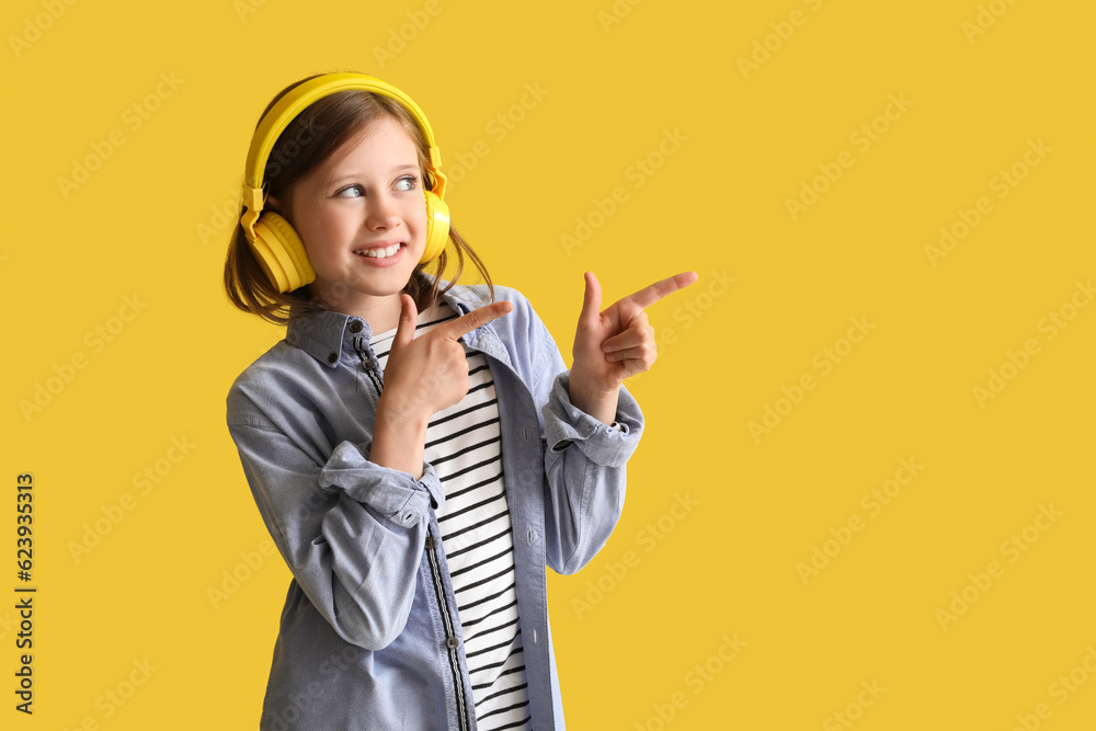 Little girl in headphones pointing at something on yellow background