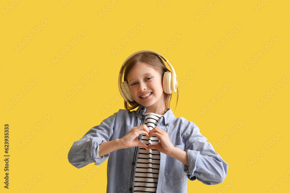 Little girl in headphones making heart gesture on yellow background