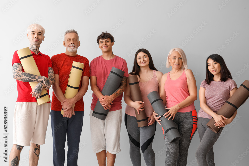 Group of sporty people with fitness mats on light background