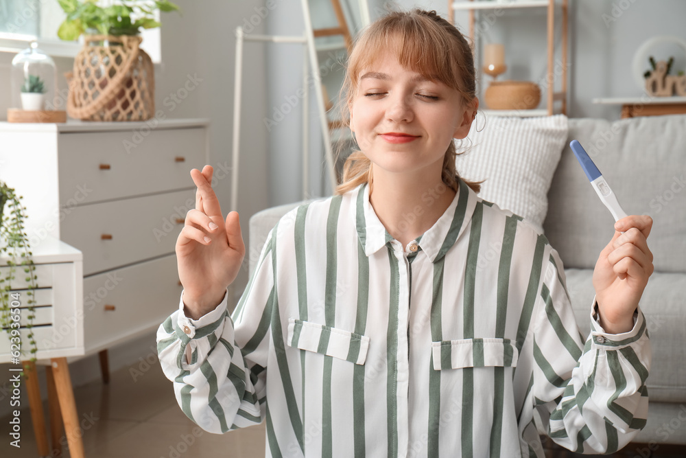 Young woman with pregnancy test crossing fingers at home