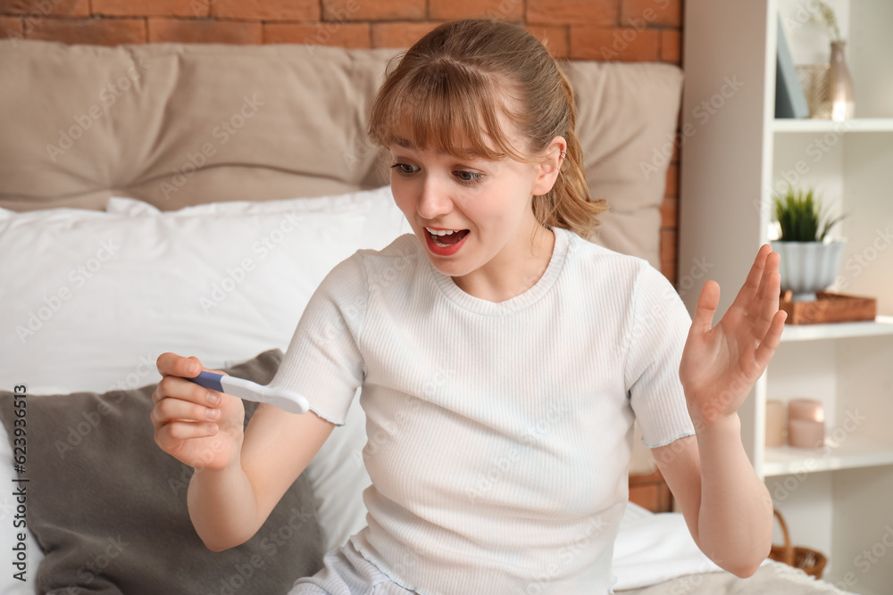 Happy young woman with pregnancy test in bedroom