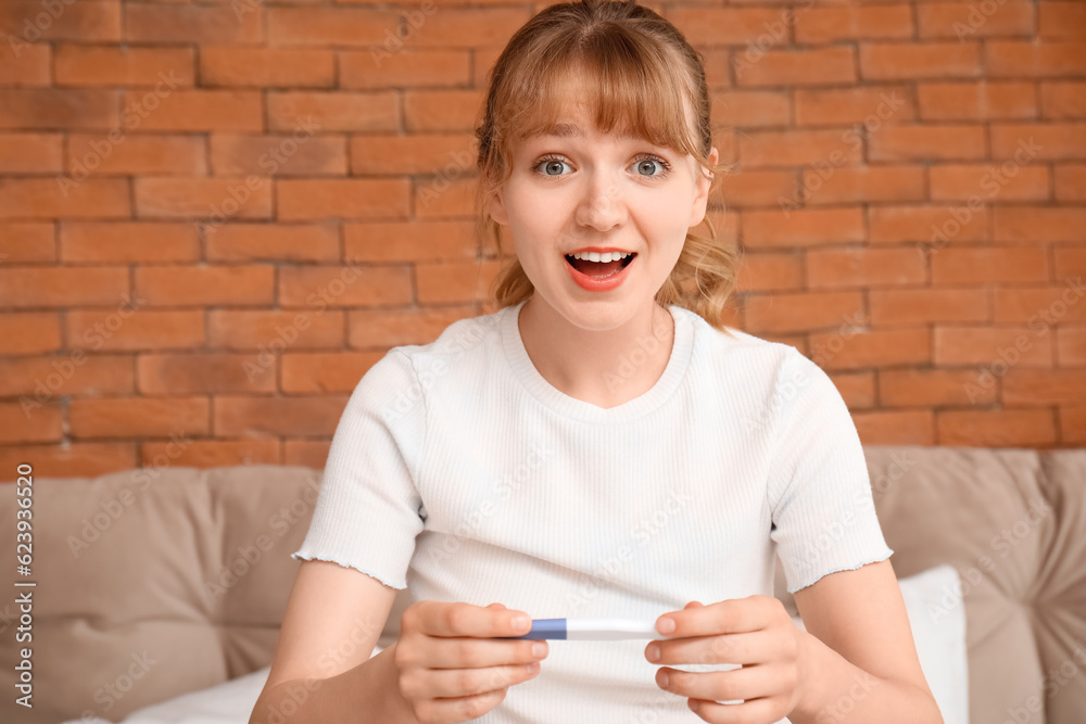 Happy young woman with pregnancy test in bedroom, closeup