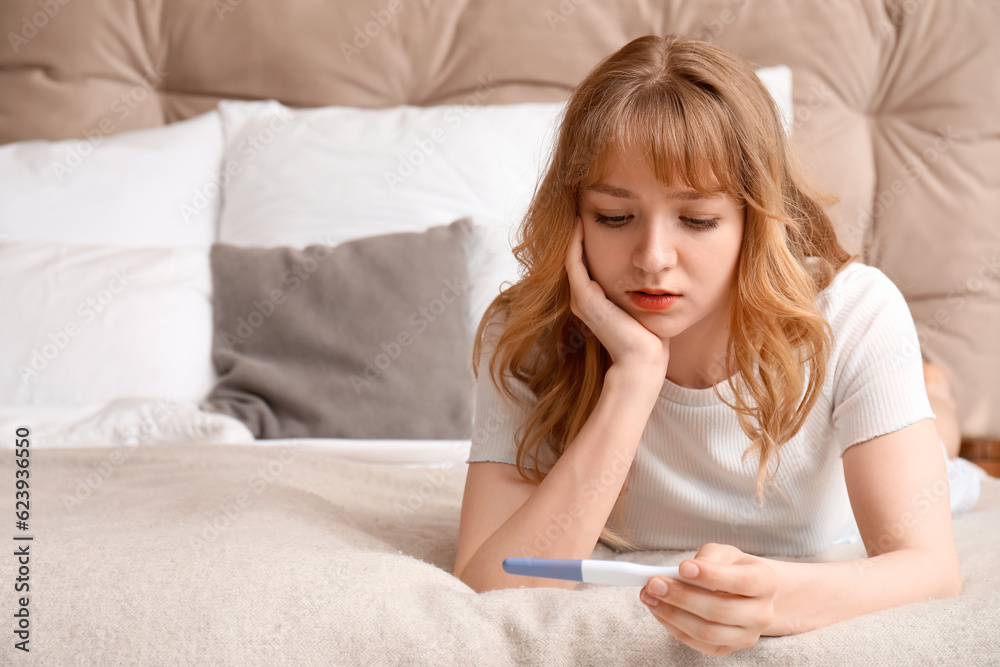 Sad young woman with pregnancy test in bedroom