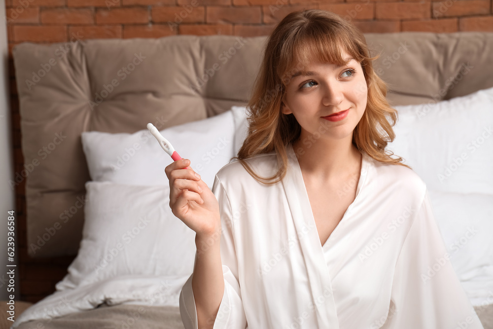 Young woman with pregnancy test in bedroom