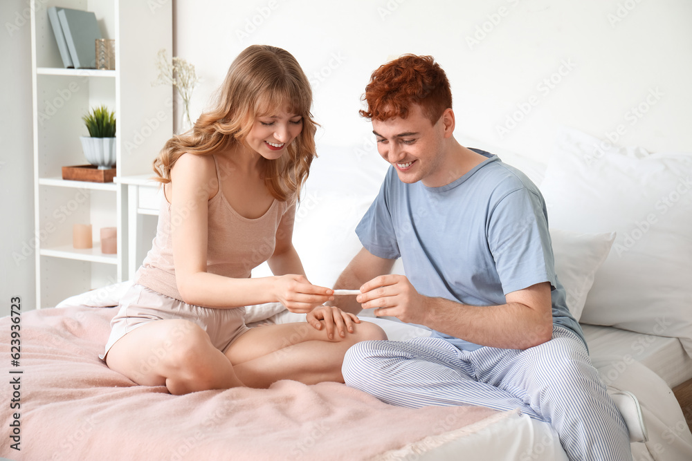 Happy young couple with pregnancy test in bedroom