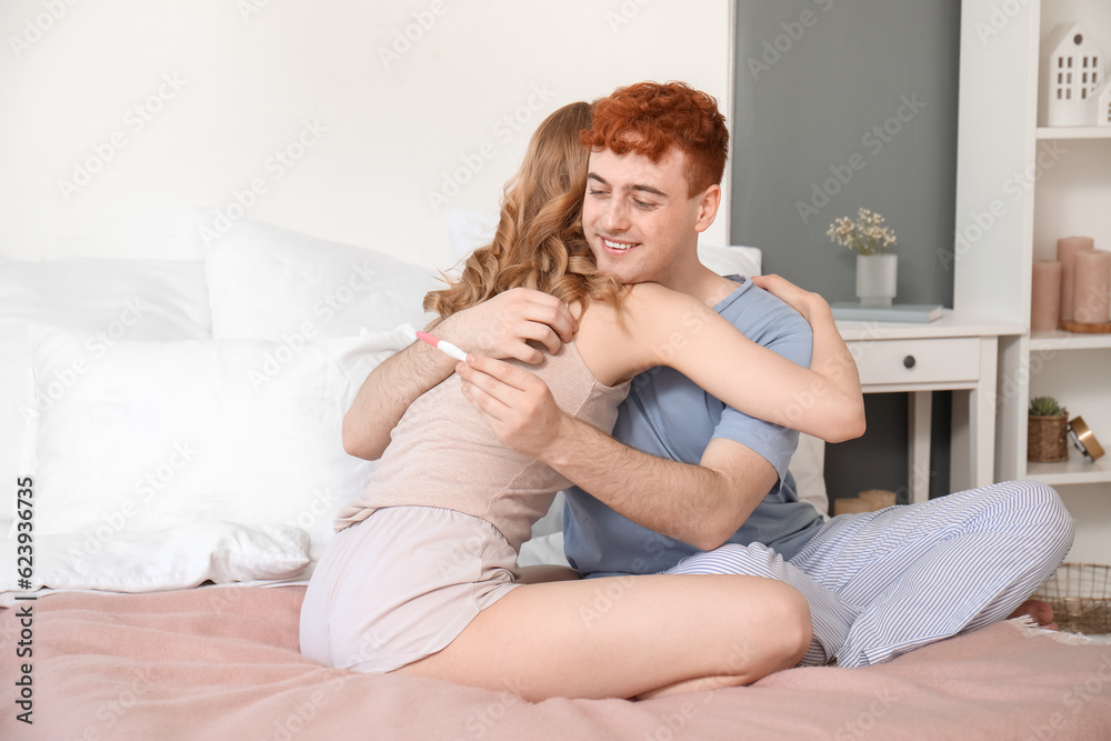 Happy young couple with pregnancy test hugging in bedroom