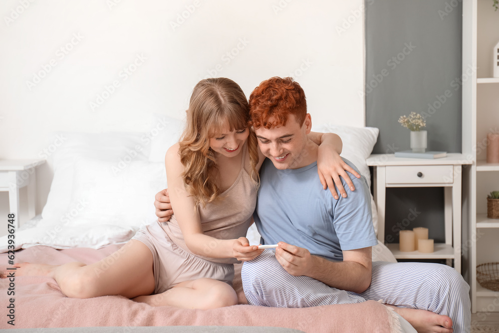 Happy young couple with pregnancy test in bedroom