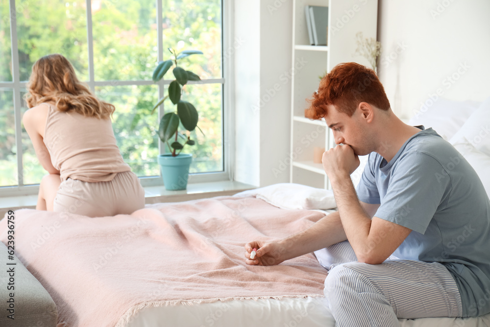 Sad young man with pregnancy test in bedroom