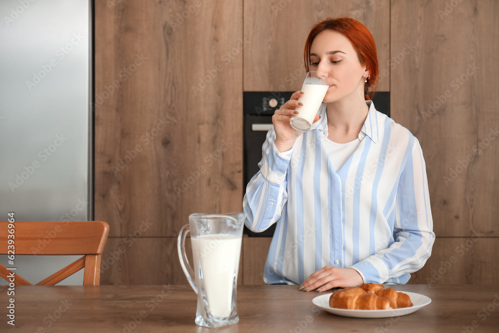 Young redhead woman drinking milk in kitchen