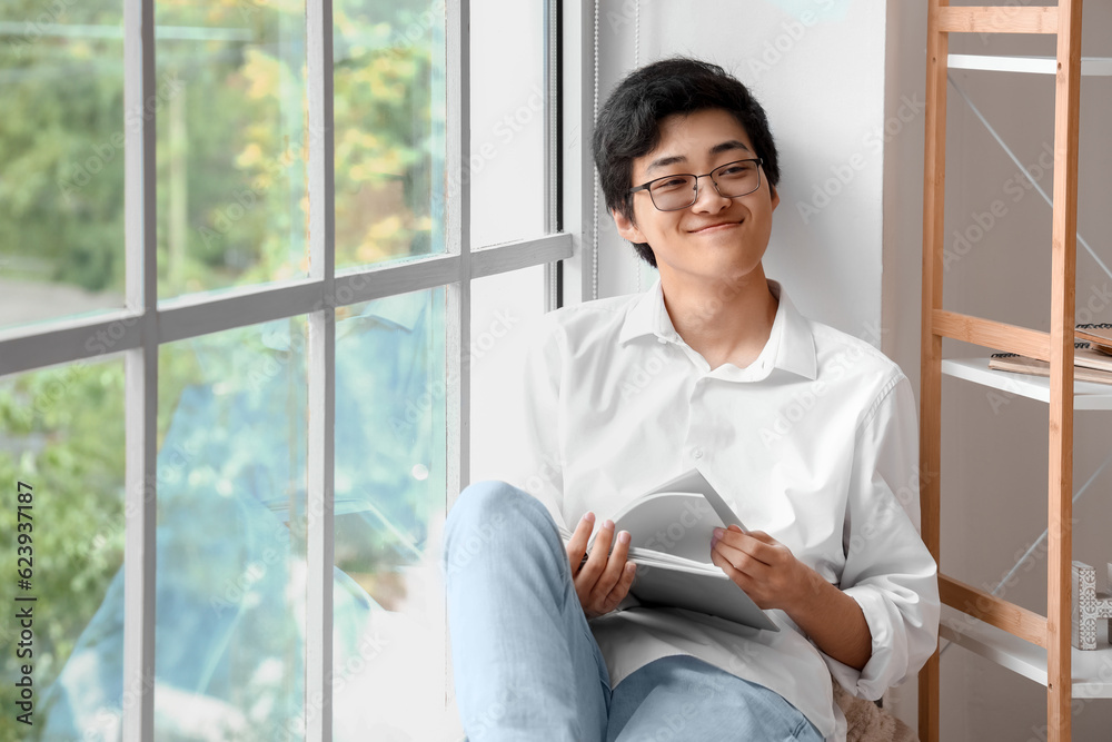 Young Asian man reading book on his day off at home