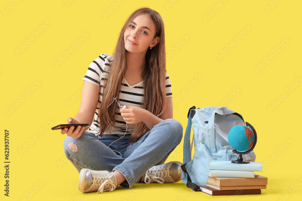 Female student in earphones with mobile phone on yellow background