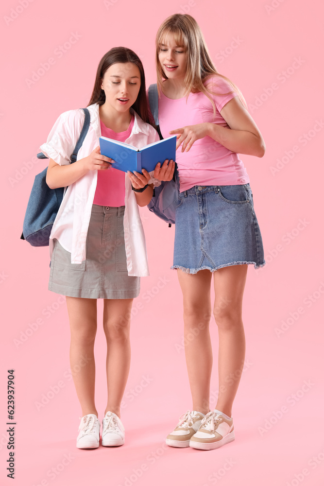 Female students reading book on pink background