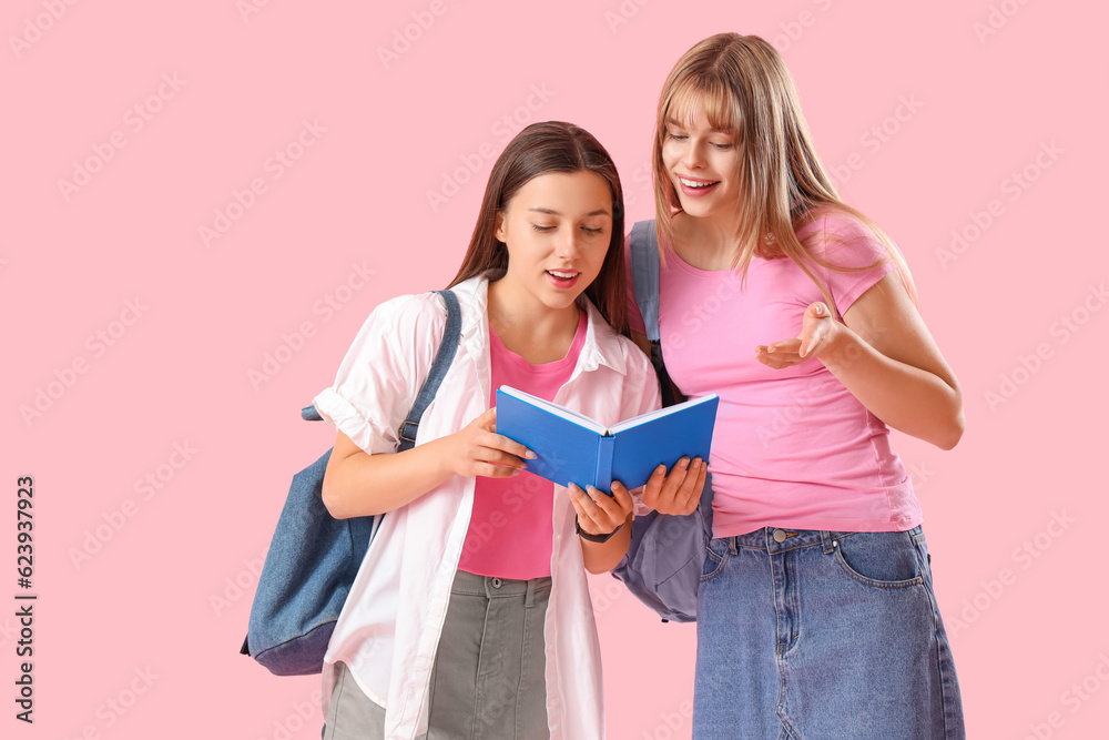 Female students reading book on pink background