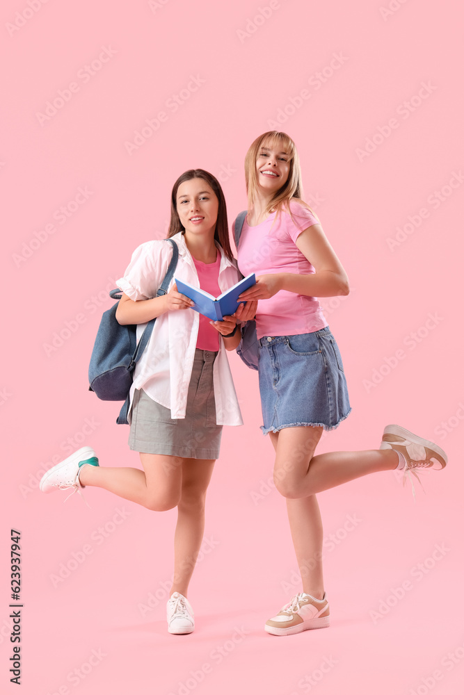 Female students reading book on pink background