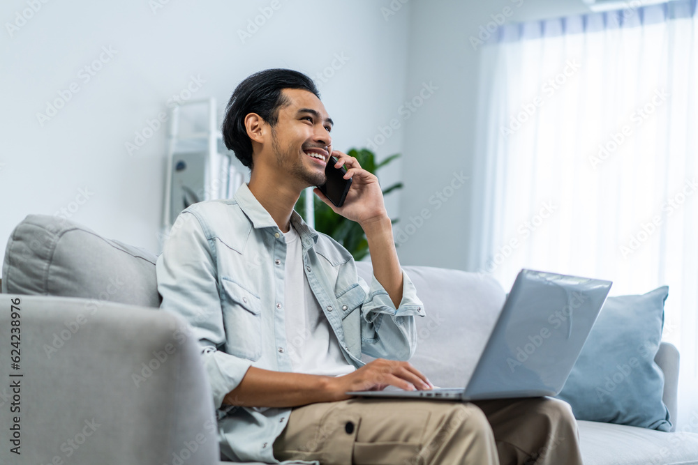 Asian young businessman typing on computer and talking on mobile phone. 