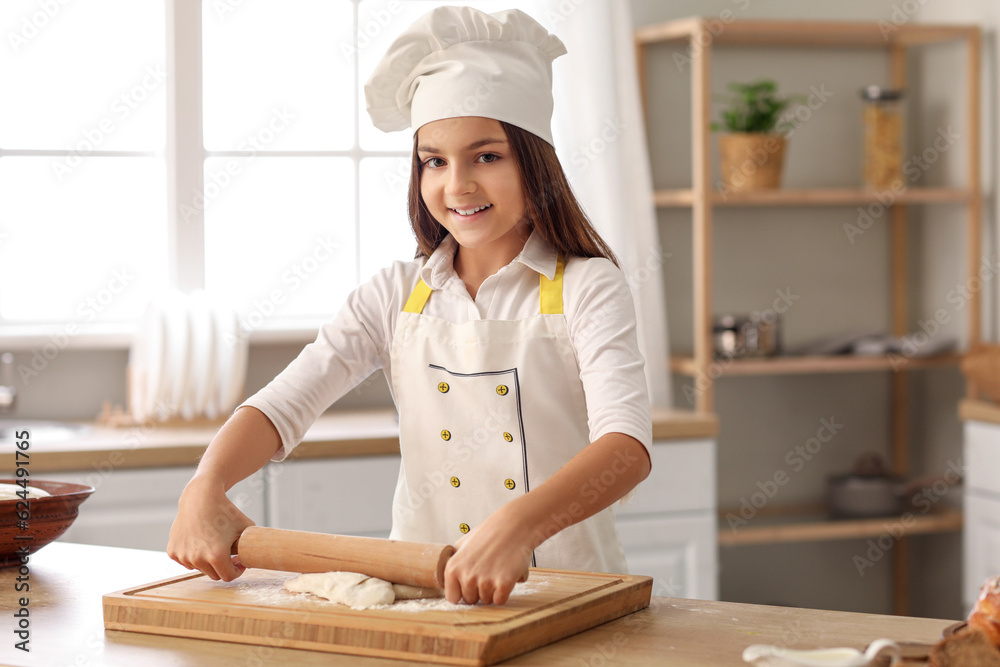 Little baker rolling out dough at table in kitchen