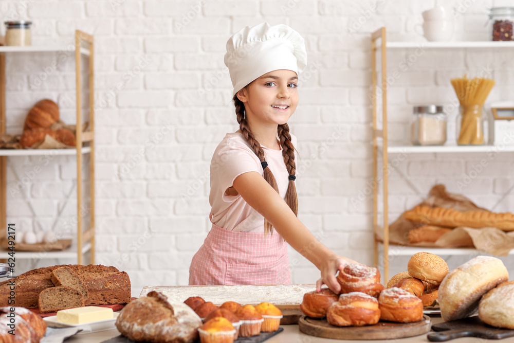 Little baker near table with tasty pastries in kitchen