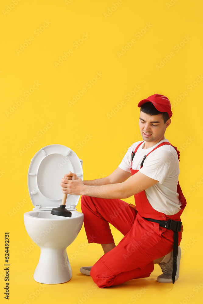 Displeased young plumber with plunger and toilet bowl on yellow background