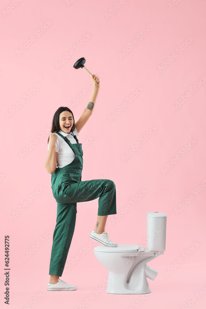 Happy female plumber with plunger and toilet bowl on pink background